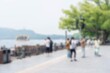 © joeycheung - Blurry image of a waterfront area with people walking and a tree in the foreground.
