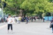 © joeycheung - A blurry image of people walking on a paved path with trees and a fence in the background.
