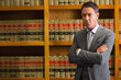 © WavebreakMediaMicro - Man standing with arms crossed in gray suit and tie at law library bookshelves, copy space