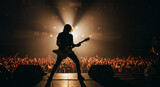 Silhouette of a guitarist performing on stage at a live music concert, playing for an energetic crowd under bright spotlights.