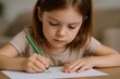 © The Little Hut - Focused Young Girl Drawing with Green Pencil on White Paper at a Wooden Table