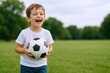 © The Little Hut - Boy Laughing While Holding a Soccer Ball in an Outdoor Park Setting, Representing Childhood Joy