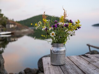 Wall Mural - rustic bouquet of wildflowers in a metal jug on a wooden table by a serene lakeside at dusk.