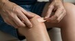 © Pluseight - Close-up of person applying adhesive bandage to scraped knee, demonstrating first aid for minor injury or wound care