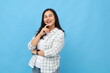 © ArvStd - Portrait of cheerful and confident young asian woman looking up in empty space, smiling, touching chin, imagining or thinking about something, wearing casual clothes, isolated on blue background.
