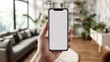 © zuriya - Hand holding an handphone with a blank screen mockup, perfect for design previews in a modern home interior
