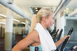 © wavebreak3 - Woman in turquoise tank top wearing gym towel exercising on elliptical machine by ducts, copy space