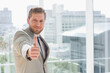 © wavebreak3 - Businessman in suit giving thumbs-up standing in office with railing viewing cityscape, copy space