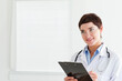 © WavebreakMediaMicro - Female doctor holding black clipboard and stethoscope in clinic room wearing lab coat copy space