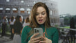 © Krakenimages.com - Young caucasian woman holding smartphone with both hands in front of coliseum building while looking at screen; amazement.