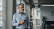 © rdkcho - Pensive Mature Businessman Leaning Against a Concrete Column with a Smartphone in an Office Setting, Contemplating the Future