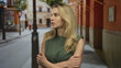 © Krakenimages.com - Woman with blonde hair appears nervous on a city street, crossing her arms while outdoors, highlighting a typical urban scene with casual attire and an engaging environment.