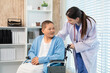 © Rakchanok - Doctor examine senior patient in clinic,  physician checkup elderly cancer illness in wheelchair, boosting trust communication, performs careful heart assessment, compassionate professional care