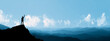© Mr.Spy - Silhouette of a triumphant man standing on a cliff edge with raised arms, overlooking a beautiful blue mountain range, symbolizing success, freedom, and adventure