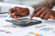 © Bapaks - Close-up of hands using calculator, charts and graphs