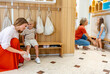 © lordn - Mother helping her son change shoes in a preschool locker area while the teacher assists another child nearby.