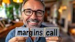 © mikail - Smiling man holding wooden blocks reading 'margins call'.