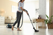 © New Africa - Woman cleaning floor with vacuum cleaner at home, closeup