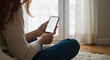 © DEGE - Woman Holding a Smartphone with a Blank White Screen Indoors Showing a Close Up View