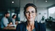 © NovaVision - A confident businesswoman in glasses smiles in a modern office setting, ready for work.