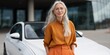 © Andrii Zastrozhnov - Mature caucasian female with long gray hair, smiling in front of a modern white car