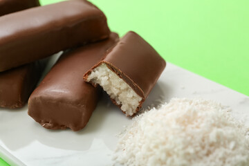 Wall Mural - Board with tasty chocolate covered coconut candies on green background