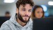 © BOJOShop - Young man with curly hair and beard smiling while looking at a computer screen