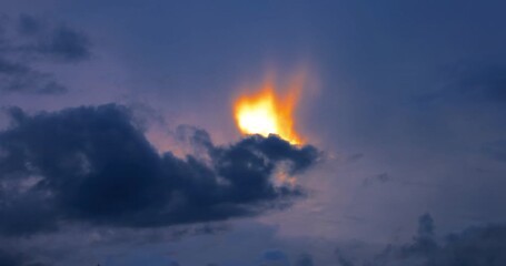 Wall Mural - bright fiery glow emerges behind dark clouds in a twilight sky, creating a dramatic mysterious scene