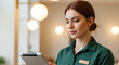 © Bakha - Confident female receptionist with name badge manages digital check in at modern front desk workspace using tablet, focused on welcoming guests and maintaining professional service