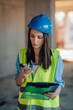 © Ljustina - Female engineer using smartphone and holding clipboard on construction site