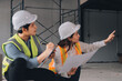 © ARMMY PICCA - Construction manager and engineer dressed in orange work vests and hard helmets explore construction documentation on the building site near the steel frames