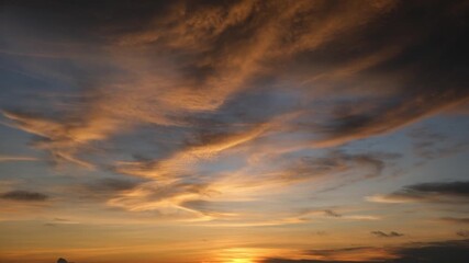 Wall Mural - A sunset sky timelapse showcasing nature’s grandeur with golden clouds gracefully swirling above, as the sun gently sets, symbolizing the peaceful rhythm and timeless beauty of the natural world.

