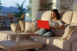 © PheelingsMedia - Woman using red laptop at sunset in a living room