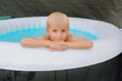 © Elena - Young Boy Relaxing in Inflatable Pool with Calm Expression