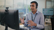 © Leny Studio - Focused Indian man at tech support call center provides professional customer service. He uses headset for video call giving helpful remote assistance to client