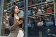 © crizzystudio - Businesswoman using smartphone and looking away near fashion store