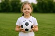 © The Little Hut - Smiling Little Girl Holding Soccer Ball Outdoors in a Grassy Field, Promoting Youth Sports