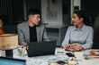 © qunica.com - Two colleagues engage in a late-night discussion at the office, collaborating on business strategies. Papers and laptops are spread across the table, showcasing teamwork and dedication.