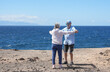 © luciano - A joyful elderly couple dances while strolling by the sea under a blue sky. Two cheerful retirees, dressed casually, radiate love and happiness, enjoying each other's company.