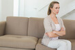 © WavebreakMediaMicro - Middle-aged woman sitting with crossed arms on beige sofa in living room by staircase, copy space