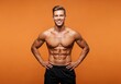 © tebu - Muscular man stands shirtless with hands on hips smiling against a solid orange background