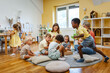 © lordn - Preschool teacher with diverse children playing and interacting on the floor in a bright classroom, encouraging teamwork, social skills, and joyful learning through play