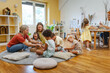 © lordn - Two preschool teachers with children sitting on floor, engaging in collaborative early learning activity in bright classroom