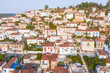 © AmazingAerialAgency - Aerial view of sun-drenched buildings with terracotta rooftops cascade down the hillside, a Mediterranean tapestry of white and earthy tones, Poros, Cephalonia, Greece.