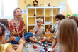 © lordn - Preschool teacher engaging a group of children in a fun music activity, sitting in a circle and playing rhythm instruments in a bright classroom
