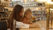© Pavel - A young mom and her daughter enjoy reading a book at the library table. An adult parent or tutor assists with school preparation and homework. The concept of private ed for children. Finland Rovaniemi