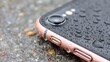 © BOJOShop - A close up view of a smartphone covered in water droplets on a wet textured surface