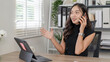 © bunyiam - A woman is talking on her cell phone while sitting at a desk