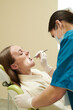 © pressmaster - Caucasian woman sitting in dental chair receiving oral examination from female dentist wearing medical gloves and mask, dentist holding dental instrument inside patient mouth
