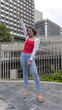© iFocus - A stylish young Asian woman with a bob haircut stands confidently in a white hoodie and a red tank top in an urban park, waving with one hand